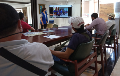 Image shows Hub and organisational members gathered at a table and listening to a presentation